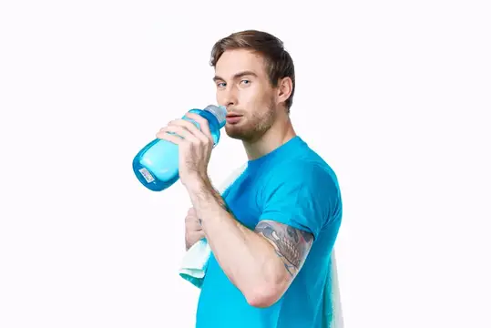 Спортивный мужчина в синей футболке с бутылкой воды, испытывающий жажду и занимающийся фитнесом