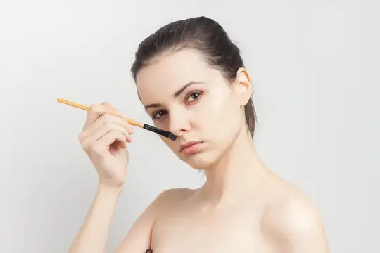 Молодая женщина наносит тени кистью на светлом фоне