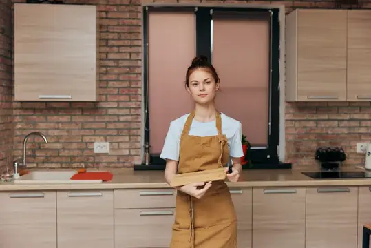 Молодая женщина в фартуке с деревянной доской на кухне