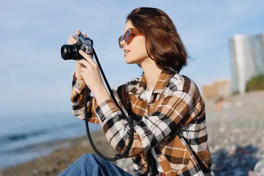 Девушка в клетчатой рубашке фотографирует на камеру у моря