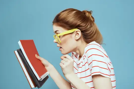 Рыжеволосая девушка в жёлтых очках удивлённо смотрит на книги