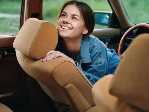 Улыбающаяся девушка в джинсовой куртке выглядывает из салона автомобиля