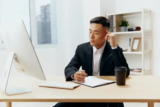 Азиатский бизнесмен в костюме задумчиво работает за столом в офисе