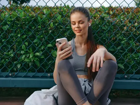 Молодая женщина в спортивной форме смотрит в телефон на улице