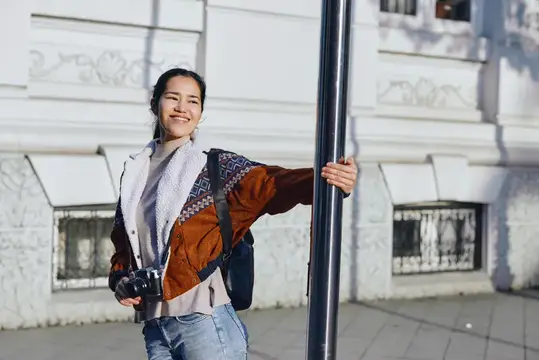 Улыбающаяся азиатская девушка с фотоаппаратом у фонарного столба