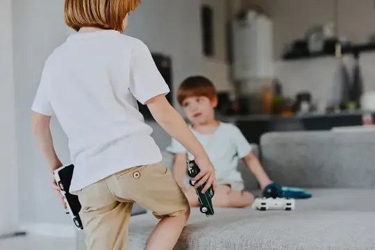 Два мальчика играют с игрушечными пистолетами в светлой гостиной