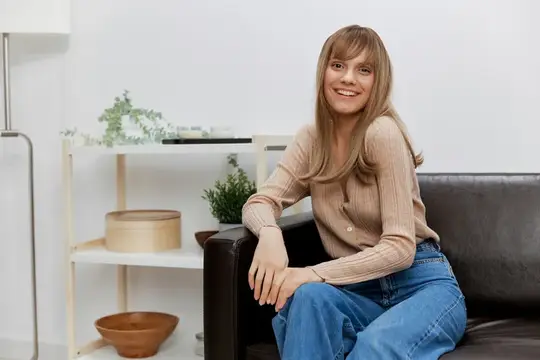 Улыбающаяся светловолосая женщина сидит на диване в светлой комнате