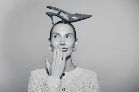 Удивленная женщина с туфлей на голове прикрывает рот рукой