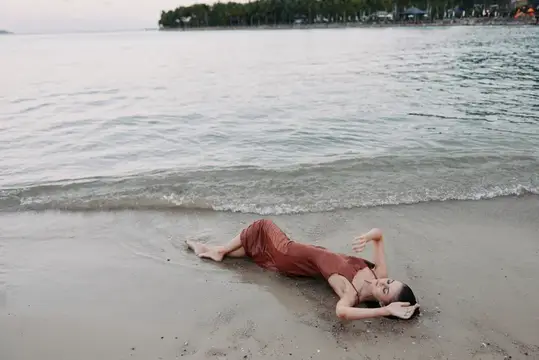 Девушка лежит на мокром песке у кромки воды