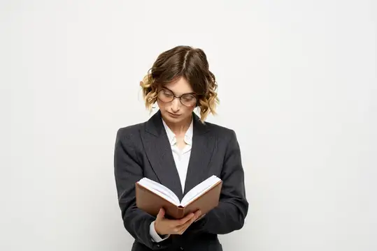 Молодая женщина в очках и деловом костюме читает книгу на белом фоне