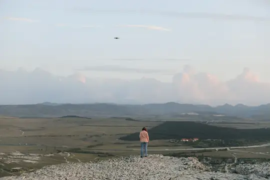 Девушка на скалистой вершине смотрит на долину и летящий самолёт