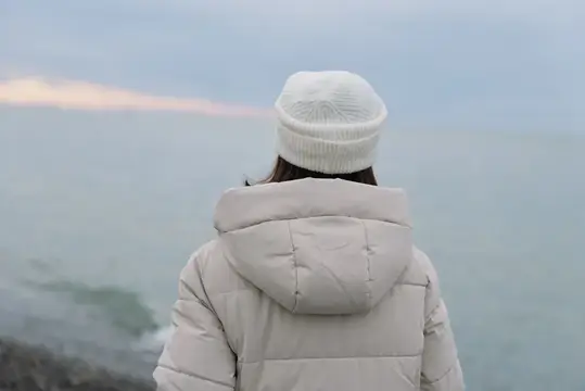 Девушка в белой шапке смотрит на море зимой
