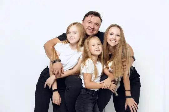 Счастливая семья с двумя дочками обнимается на белом фоне