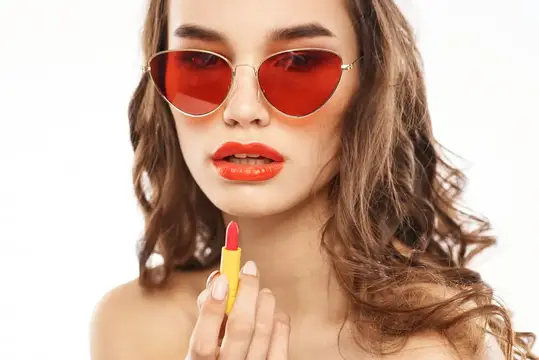 Молодая женщина в красных солнцезащитных очках держит красную помаду