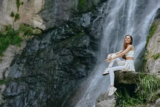 Улыбающаяся девушка отдыхает на камне у водопада