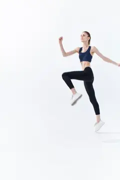 Молодая женщина в спортивной форме прыгает на белом фоне