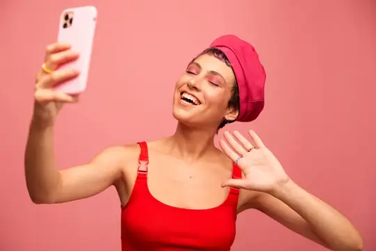 Улыбающаяся девушка в красном делает селфи на розовом фоне