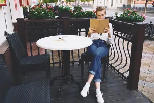 Молодая женщина читает книгу за столиком летнего кафе