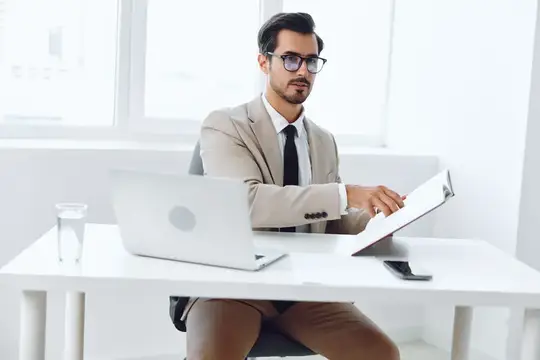 Мужчина в очках и бежевом пиджаке работает за ноутбуком в офисе