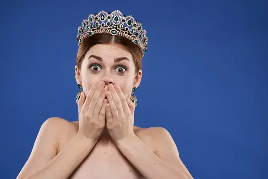Красивая женщина в короне на голове, модель с макияжем, делает жест рукой на изолированном фоне