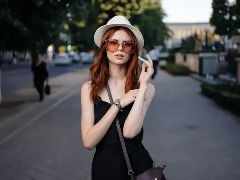 Симпатичная женщина в платье и шляпе с сумкой на плече идет по улице