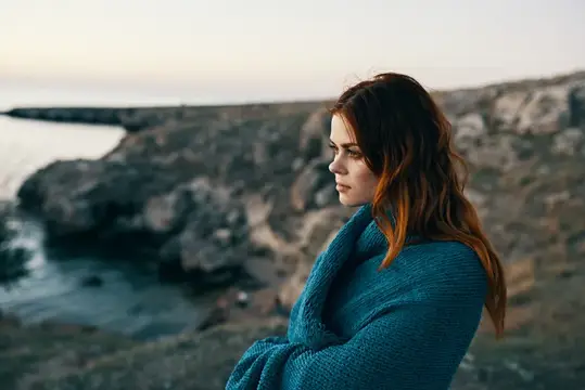 Женщина на закате у моря в горах с пледом на плечах