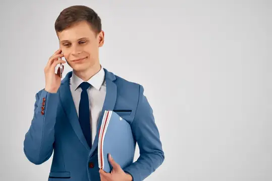 Молодой человек в синем костюме говорит по телефону с папкой