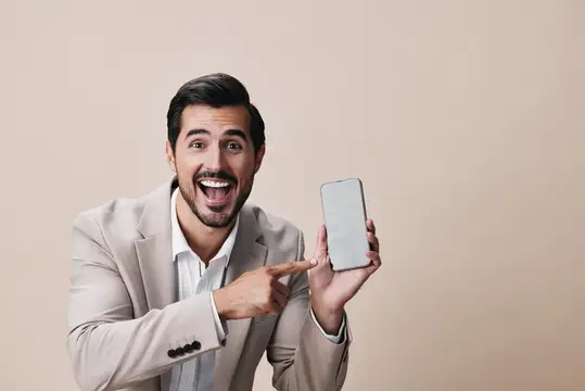 Удивлённый мужчина в бежевом пиджаке показывает на смартфон