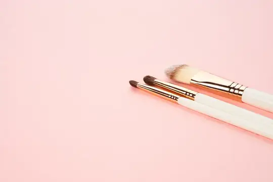 Три кисти для макияжа лежат на нежно-розовом фоне
