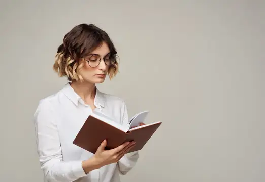 Молодая женщина в очках с книгой в руках на сером фоне