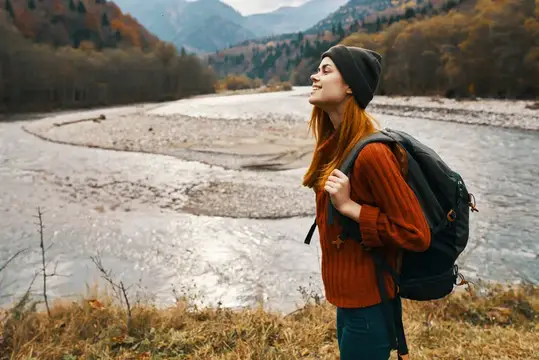 Рыжеволосая девушка с рюкзаком любуется горной рекой осенью