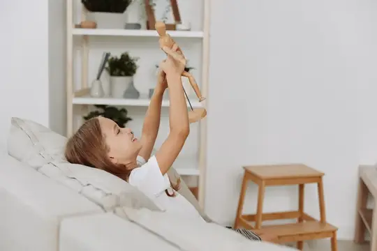 Мальчик лежит на диване и играет с деревянной куклой