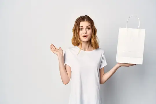 Удивлённая девушка с белой бумажной сумкой на светлом фоне