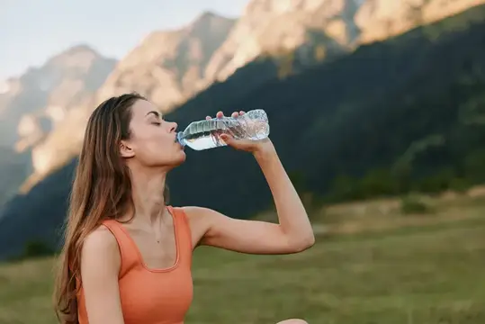 Молодая женщина пьёт воду из бутылки на фоне гор