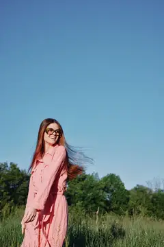 Улыбающаяся девушка в розовом платье и очках на фоне поля и неба