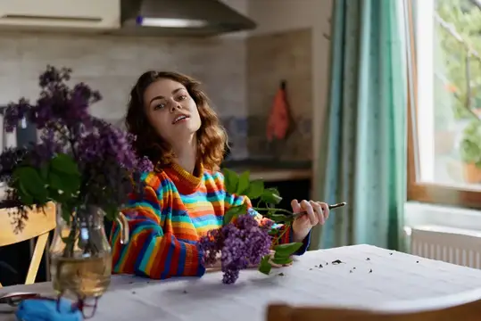 Молодая женщина в полосатой кофте с сиренью на кухне
