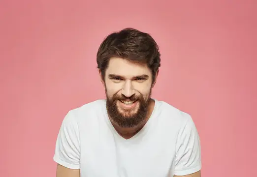 Улыбающийся бородатый мужчина в белой футболке на розовом фоне