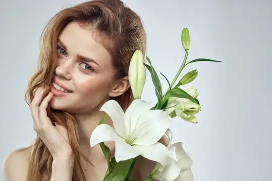 Рыжеволосая девушка с белыми лилиями нежно улыбается на светлом фоне