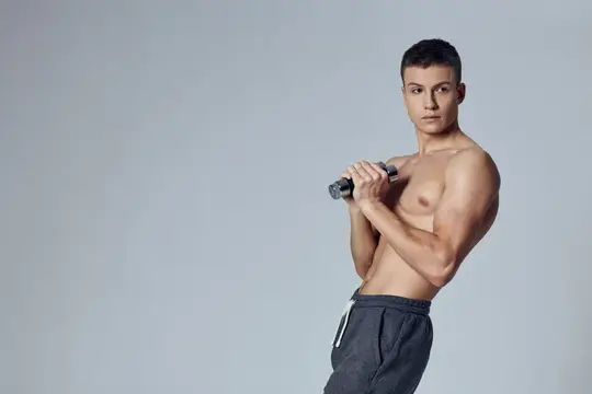 Молодой спортивный парень с гантелью на сером фоне
