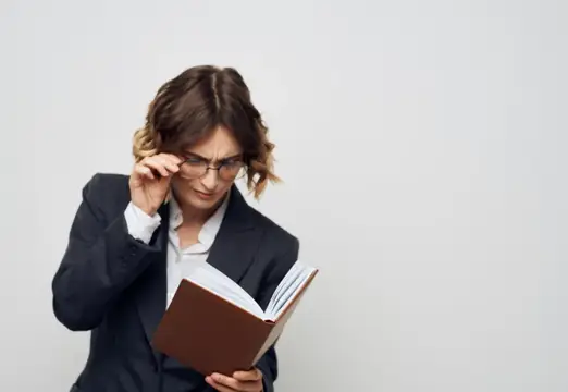 Женщина в очках и деловом костюме сосредоточенно читает книгу
