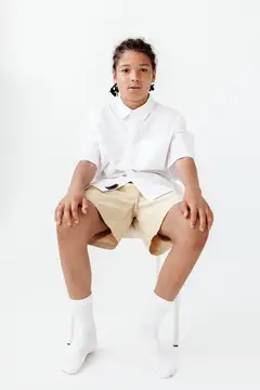 Темнокожий мальчик в белой рубашке и шортах сидит на стуле