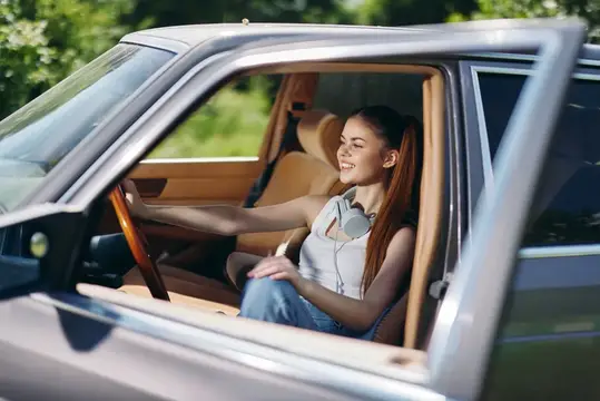 Улыбающаяся девушка за рулём автомобиля в солнечный день