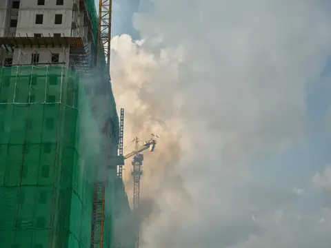 Строящееся здание в зелёной сетке и башенный кран в облаке пыли