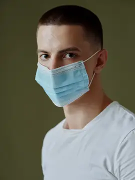 Молодой человек в медицинской маске смотрит прямо в камеру