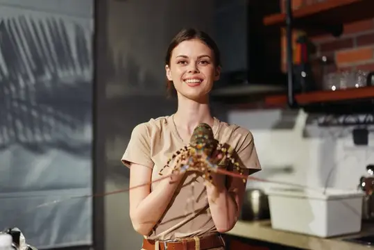 Улыбающаяся девушка держит живого лангуста на кухне