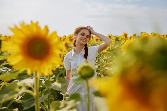 Женщина с косичками стоит в поле подсолнухов на фоне живописного пейзажа