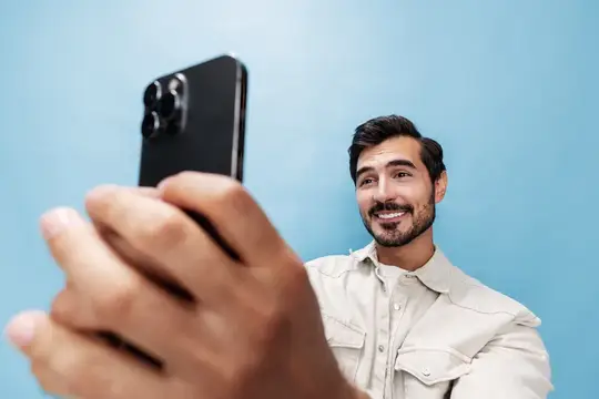 Улыбающийся бородатый мужчина делает селфи на смартфон на голубом фоне
