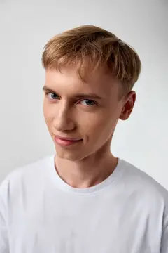 Молодой блондин с лёгкой улыбкой на сером фоне