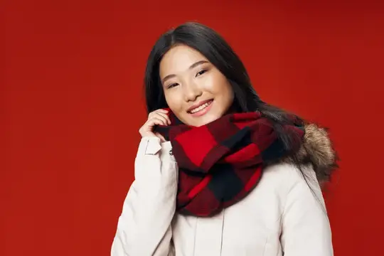 Улыбающаяся азиатская девушка в клетчатом шарфе на красном фоне