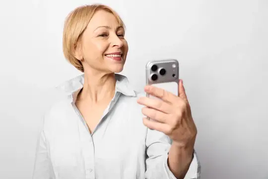 Улыбающаяся блондинка в белой рубашке смотрит в смартфон
